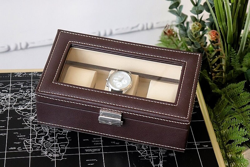 Элегантные наручные часы в элегантном коричневом кожаном футляре лежат на столике с изображением карты мира.